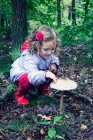 Ragazza sorridente che tocca un fungo che cresce nella foresta, Polonia — Foto stock