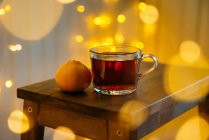 La taza del té y la mandarina sobre la mesa con las decoraciones de hadas claras - foto de stock