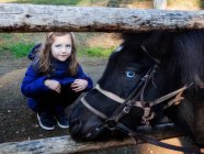 Retrato de una chica agachada junto a un caballo - foto de stock