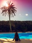 Visão traseira de uma menina sentada na borda de uma piscina — Fotografia de Stock