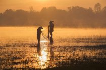 Silhouette de deux pêcheurs jetant des filets de pêche au coucher du soleil, Thaïlande — Photo de stock