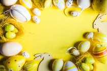 Пасхальне яйце та прикраси великодніх кроликів розташовані на жовтому тлі — стокове фото