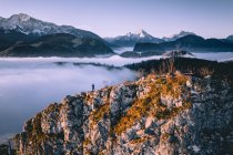 Hombre de pie en la cresta de la montaña elevándose por encima de la alfombra de nubes, Hallein, Salzburgo, Austria - foto de stock