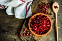 Overhead view of a bowl of pomegranate seeds on a wooden chopping board with a wooden spoon — Stock Photo
