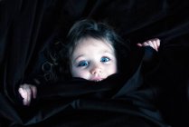 Portrait of a smiling girl hiding under bed sheets — Stock Photo