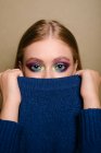 Portrait of a beautiful woman with striking eye make-up holding a sweater over part of her face — Stock Photo