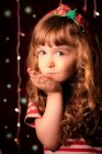 Portrait d'une fille souriante qui souffle des baisers devant les lumières de Noël — Photo de stock
