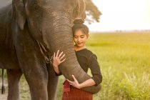 Porträt einer Frau, die mit einem Elefanten auf einem Reisfeld steht, Thailand — Stockfoto
