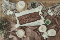 Vue aérienne du gâteau au chocolat avec des bougies, des plantes et une casserole de crème — Photo de stock