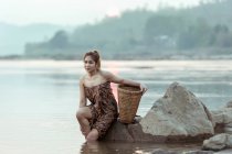 Mujer sentada en una roca junto a un río, Tailandia - foto de stock