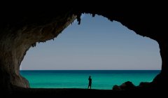 Silhouette of a woman standing on beach from inside a cave, Sardinia, Italy — Stock Photo