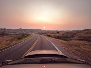 Coche conduciendo a lo largo de la carretera al atardecer durante incendios forestales, Parque Nacional Badlands, Dakota del Sur, EE.UU. - foto de stock