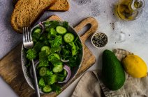 Gesundes grünes Salatkonzept mit Eisbergsalatblättern, Gurke, Sesamöl und Samen in einer Schüssel — Stockfoto