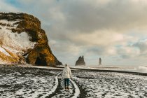 Женщина идет вдоль черного песчаного пляжа в снегу, Исландия — стоковое фото