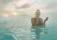 Woman standing in the Blue Lagoon putting mud on her face, Iceland — Stock Photo