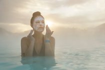 Frau steht in der Blauen Lagune und legt sich Schlamm ins Gesicht, Island — Stockfoto
