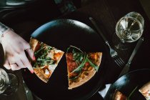 Overhead view of a woman reaching for a slice of pizza — Stock Photo