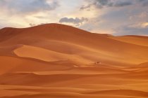 Dos personas caminando por el paisaje del desierto cerca de Merzouga al atardecer con camellos, Marruecos - foto de stock