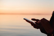 Nahaufnahme einer Frau mit einem Mobiltelefon auf dem Meer bei Sonnenuntergang, Weißrussland — Stockfoto