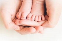 Primer plano de una madre sosteniendo los pies de su hijo en sus manos - foto de stock