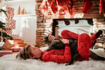 Garçon couché sur un tapis moelleux caressant son chat — Photo de stock