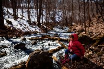 Boy sitting by a frozen lake in early spring, USA — Stock Photo
