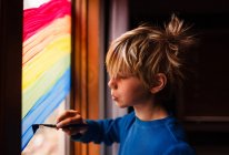 Boy painting a rainbow on a window, USA — Stock Photo