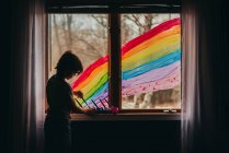 Garçon peignant un arc-en-ciel sur une fenêtre, États-Unis — Photo de stock