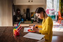 Mädchen sitzt in der Küche und bemalt einen Regenbogen — Stockfoto