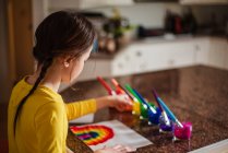 Девушка, сидящая на кухне и рисующая радугу — стоковое фото