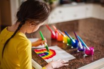 Ragazza seduta in cucina che dipinge un arcobaleno — Foto stock