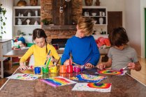 Троє дітей сидять на кухні малюють веселку — стокове фото