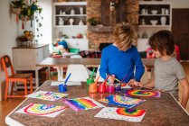Dos chicos sentados en la cocina pintando un arco iris - foto de stock