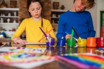Двое детей сидят на кухне и рисуют радугу. — стоковое фото