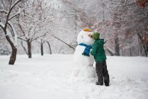 Niño de pie en el bosque haciendo un muñeco de nieve, EE.UU. - foto de stock