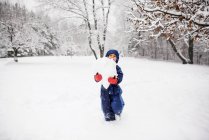 Menino carregando uma bola de neve gigante para fazer um boneco de neve, EUA — Fotografia de Stock