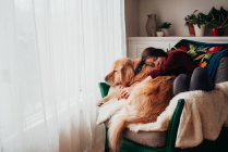 Girl sitting in an armchair cuddling her dog — Stock Photo