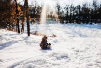 Niño bajando en trineo por una colina en la nieve, EE.UU. - foto de stock