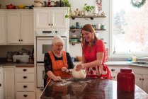 Старшая женщина учит свою дочь печь хлеб — стоковое фото