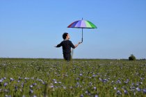 Человек, стоящий на льняном поле с разноцветным зонтиком, Франция — стоковое фото