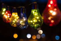 Multi coloured light bulbs hanging in a row at night — Stock Photo