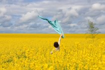 Frau steht in einem Rapsfeld und hält ihren Schal in die Luft, Frankreich — Stockfoto