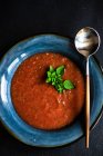 Sopa de crema de tomate con orégano servido en un tazón y cubiertos sobre fondo de hormigón con espacio para copiar - foto de stock