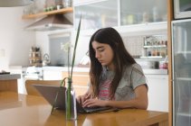 Ragazza adolescente seduta in cucina con un computer portatile — Foto stock