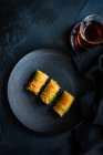 Famous turkish or oriental delight Baklava served with black tea on black dishware and black concrete background — Stock Photo