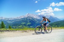 Mujer montando bicicleta de montaña frente al paisaje alpino de montaña, - foto de stock
