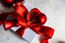 Caixa de presente embrulhada amarrada com uma fita vermelha e bugigangas de Natal — Fotografia de Stock