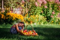 Portrait of a smiling girl sitting in a garden next to a basket of fresh tomatoes, USA — Stock Photo