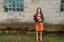 Menina sorridente em pé em uma fazenda segurando um frango, EUA — Fotografia de Stock