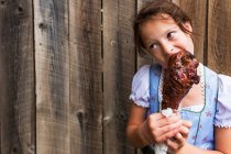 Menina em pé por uma cerca comendo uma perna de peru grelhado, EUA — Fotografia de Stock